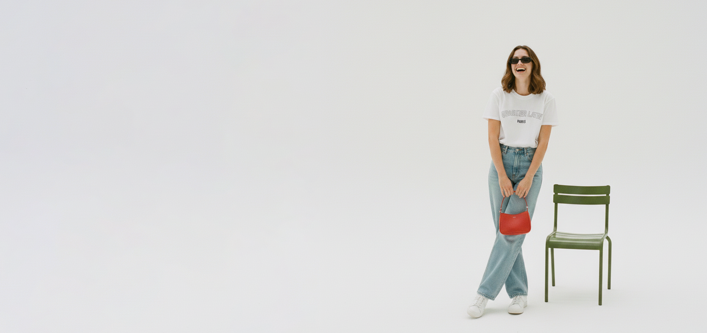 Model in white studio posing in a Quartier Latin Paris souvenir t-shirt by Kaiaer & Schmarrn Clothing, holding a red handbag next to a green park chair.